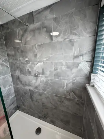 Grey tiled shower enclosure with a glass screen and white tray