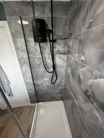 White shower tray and black shower fittings inside a tiled enclosure