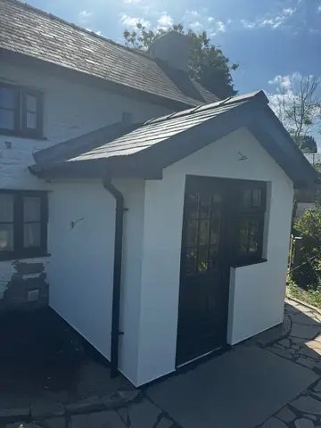 Angled view of a white porch with a dark door and pitched roof