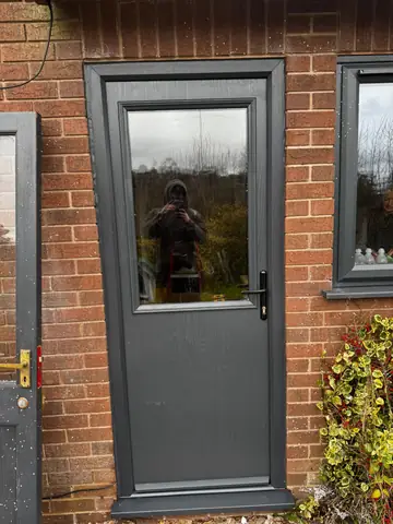 Dark external door with glazed upper panel in a brick doorway