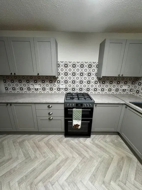 Completed grey kitchen with patterned splashback, cooker and herringbone flooring